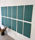 Ten rectangular teal-green acoustic panels arranged in two rows of five on a white wall, with a small woven basket and dried grasses at the lower left.