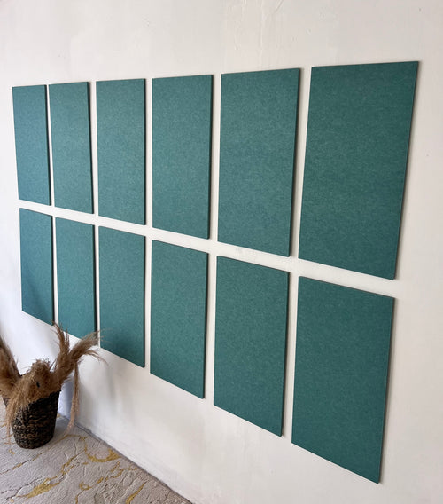 Ten rectangular teal-green acoustic panels arranged in two rows of five on a white wall, with a small woven basket and dried grasses at the lower left.